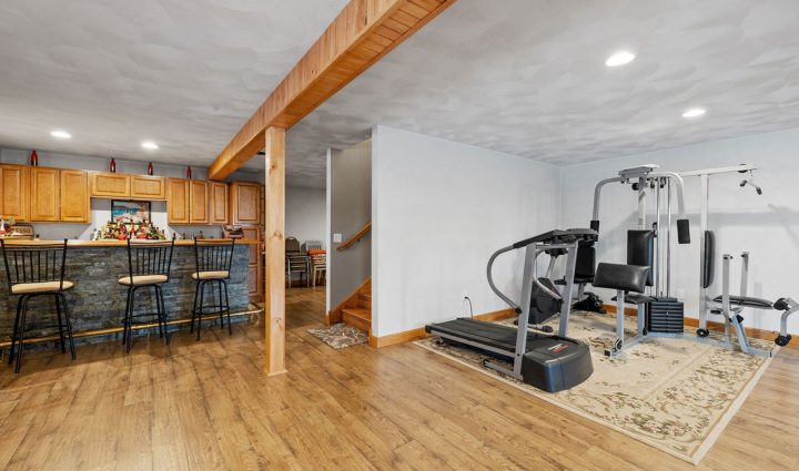 A multi-functional basement space equipped with a home gym including treadmills and weight stations, adjacent to a cozy bar area with wooden cabinetry and modern bar stools