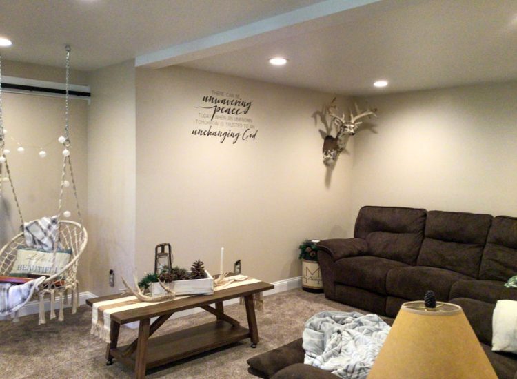 Renovated basement space with decorative hanging chair, wall art quoting "unwavering peace," and elegant rustic décor.